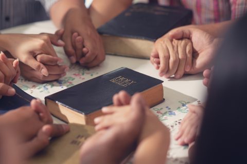 Christians  and Bible study concept. Group of discipleship Studying the Word Of God in church and Christians holding each others hand praying together (Christians  and Bible study concept. Group of discipleship Studying the Word Of God in church and C